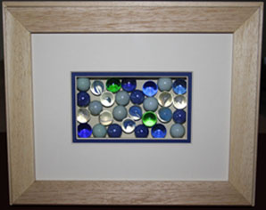 The marbles are contained in a box made from foam board lined with mount board and covered with a piece of glass before adding a double mount.